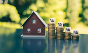 symbol for decreasing interest rates. dice with percentage symbols on decreasing high stacks of coins next to a model house.